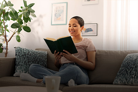 Foto de uma mulher sentada em um sofá sorridente lendo livro