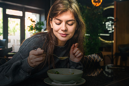 Ao fundo imagem de uma mulher prestes a comer uma sopa